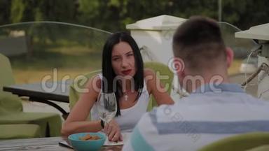 一个漂亮的女人和一个男人坐在一个开放的露台上的餐馆的桌子旁。